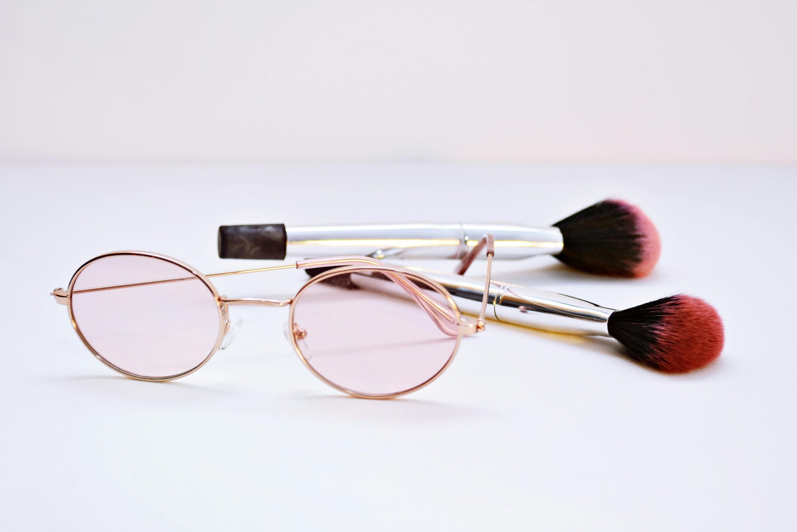Stylish eyeglasses with pink lenses and makeup brushes on a neutral background.