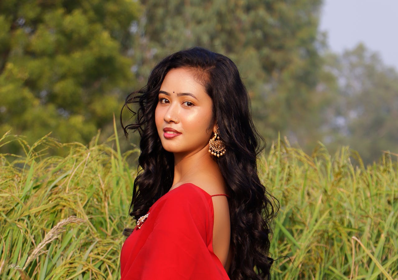 A beautiful South Asian woman poses in a red saree against a lush outdoor background in Janakpur, Nepal.