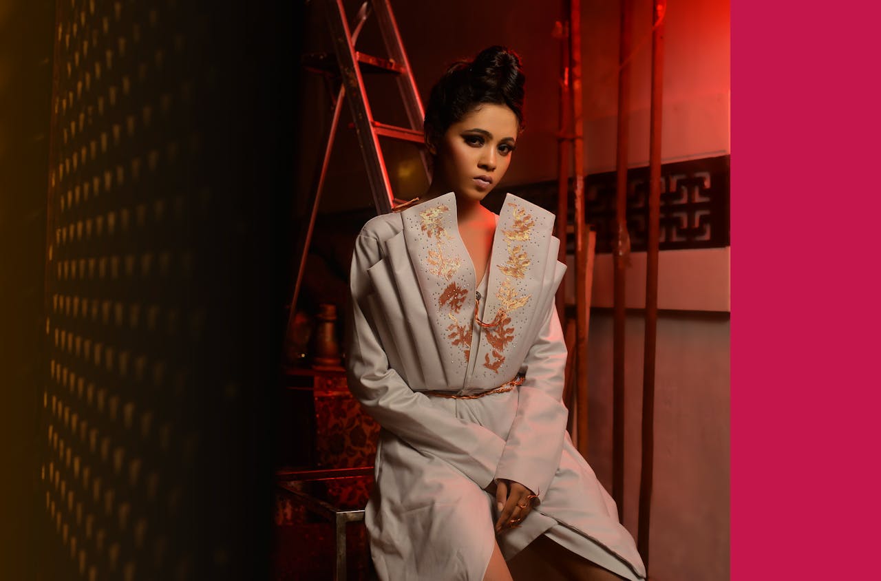 Elegant woman posing indoors in a white embroidered dress with stylish hairstyle and makeup.