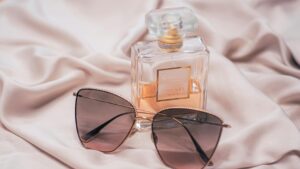 Stylish Coco Chanel perfume and sunglasses arrangement on silk fabric.